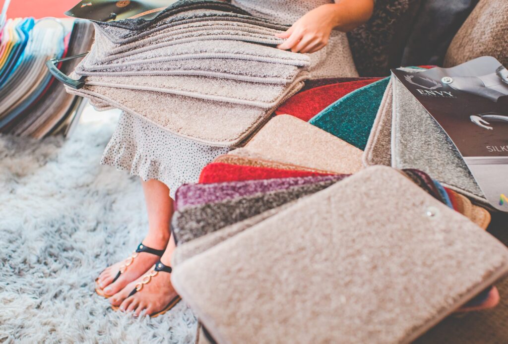 A close-up view of a person browsing through a wide variety of carpet samples in various colours like beige, red, teal, and grey during an at-home flooring consultation in Marlborough.